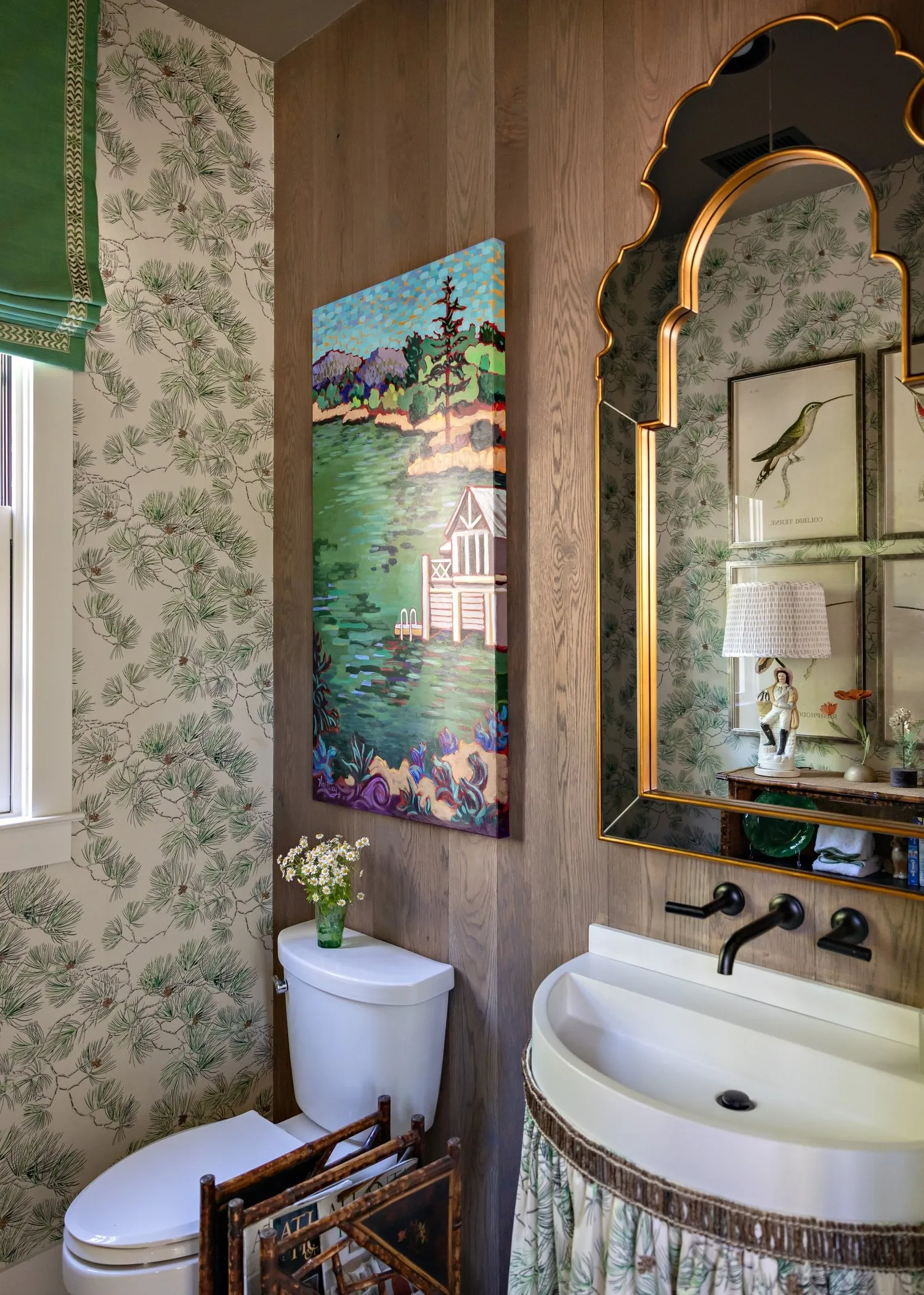 A powder room in pine-sprig paper and oak boards, a gilt arched mirror over a skirted basin.
