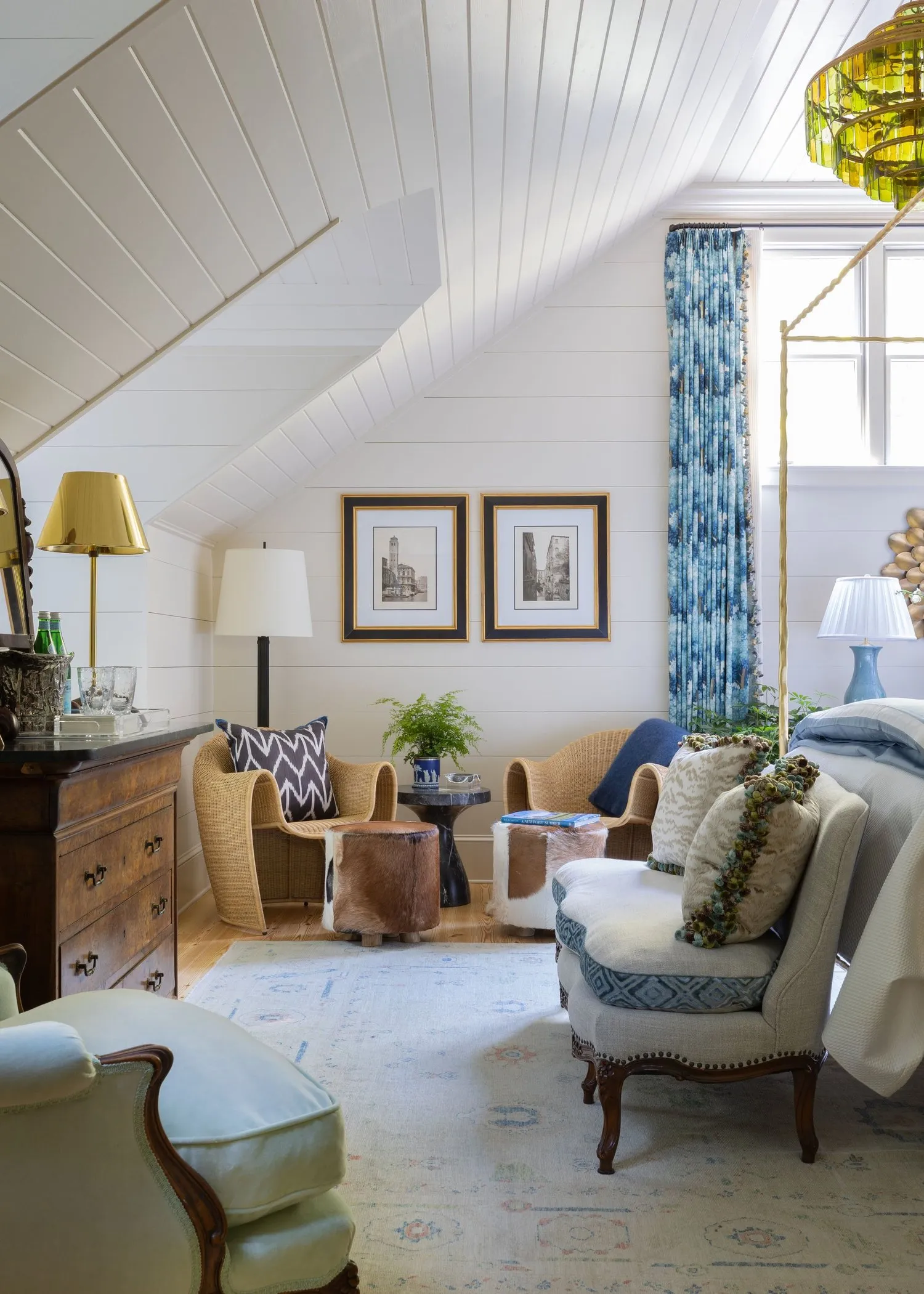 An attic bedroom under white-painted boards, with blue printed curtains and a pair of rattan chairs.