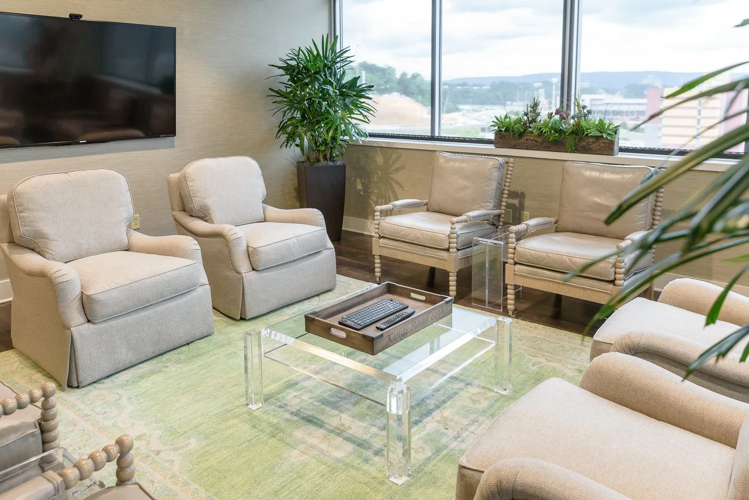 An office sitting area of linen armchairs around an acrylic table, the city through the windows behind.